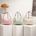 Three quilted handbags in pink, green, and white on a white surface with a lamp in the background.