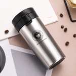 Silver thermos with black lid on a light surface with coffee beans
